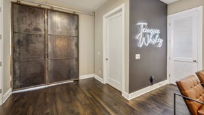 A room with a dark wood floor, a sliding door, a neon sign reading "Tennessee Whiskey", and a chair.