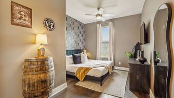 A bedroom with a bed, a ceiling fan, a wooden barrel, a lamp, a mirror, and a wall with a logo.