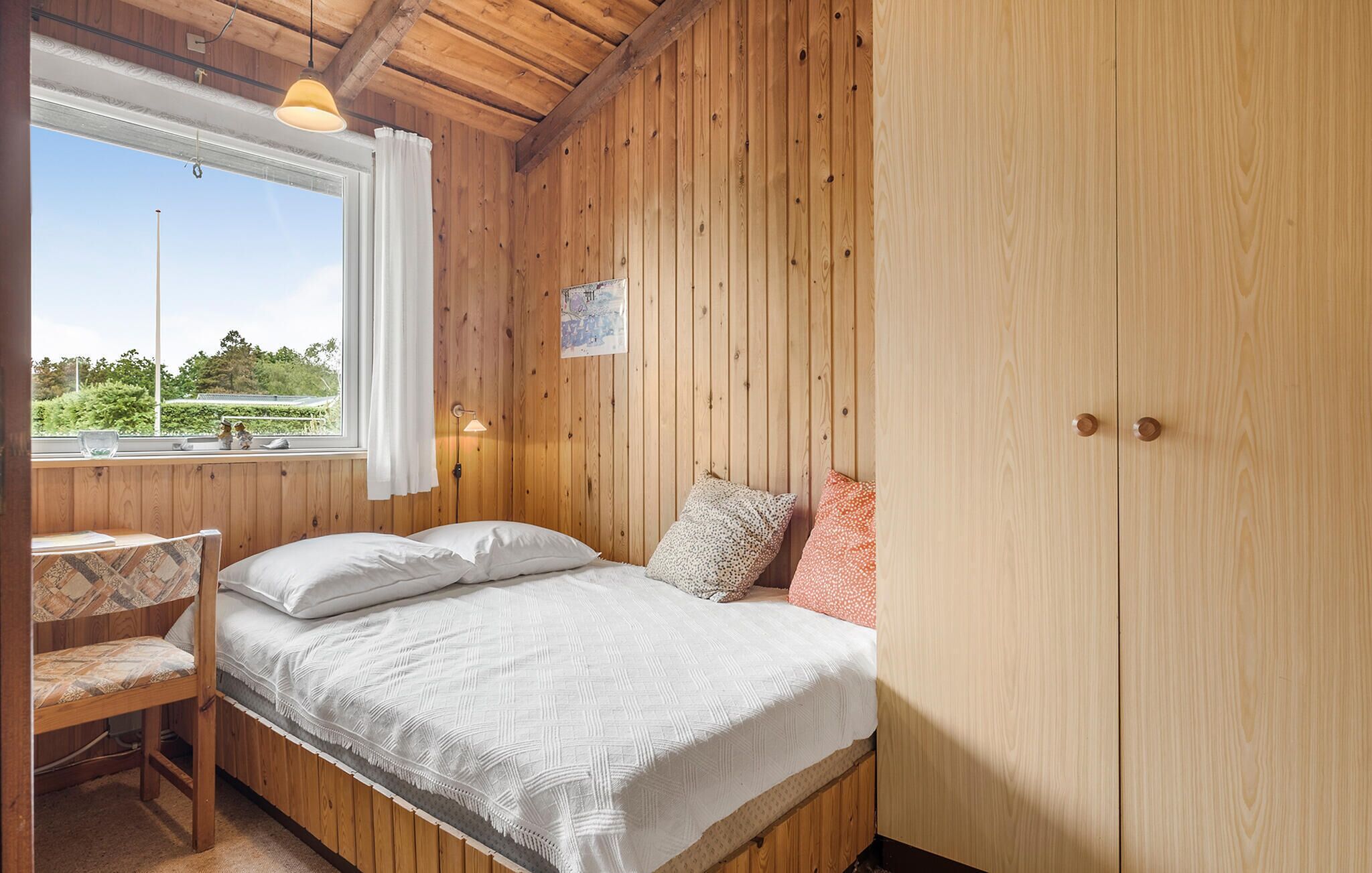 A wooden room with a bed, a desk, and a window.