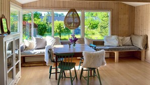 A room with a wooden ceiling, large windows, a dining table, chairs, a bench, and a hanging light fixture. - Holiday home close to the beach in Nødebohuse (Hundested)
