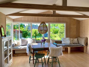 A room with a wooden ceiling, large windows, a dining table, chairs, a bench, and a hanging light fixture. - Holiday home close to the beach in Nødebohuse (Hundested)