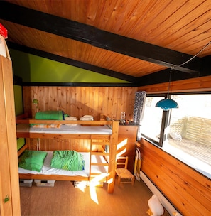 A wooden cabin with bunk beds, a small desk, and a window with a view.