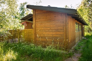Een houten blokhut met schuin dak, een klein terras en een pad naar de ingang.