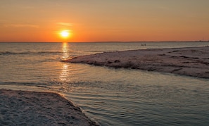 A sunset over a beach with calm water and a rocky shoreline.