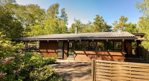 A wooden cabin with a tiled roof, surrounded by lush greenery and trees.