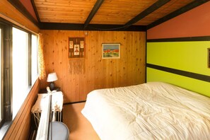 Een kamer met houten wanden, een bed, een tafeltje met een lamp en een raam met gordijnen.