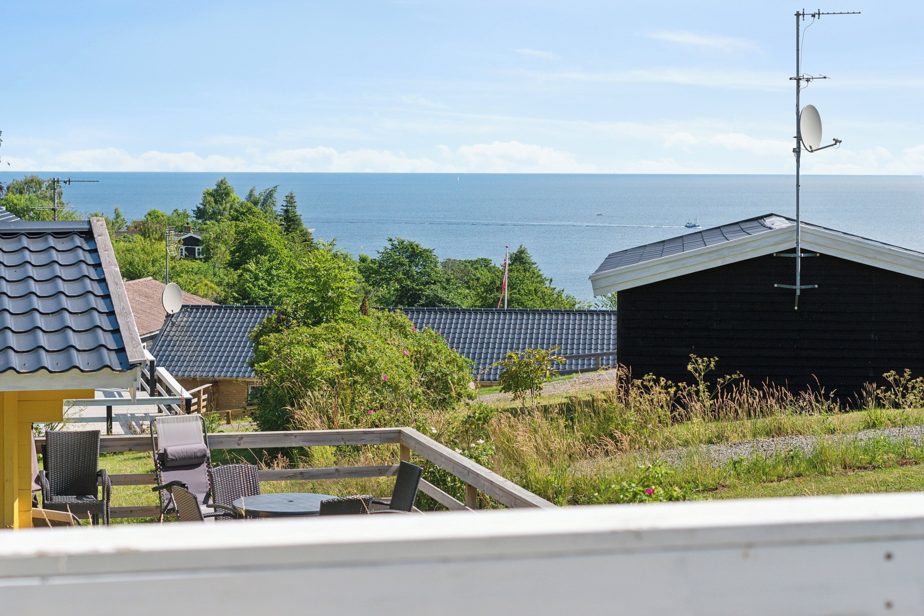 Blick auf die Küste mit einer Satellitenschüssel, einer Holzterrasse mit Stühlen und einem Gebäude mit dunklem Dach.