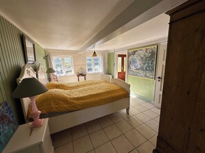 Ein Schlafzimmer mit Bett, Nachttisch, Lampe, Kommode und Fenster.