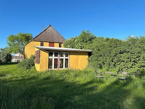 Ein gelbes Gebäude mit rotem Dach, großen Fenstern und einem kleinen Anbau.