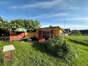 Un petit bâtiment d’un seul étage, à la façade jaune et rouge, avec un parasol vert et un portail en métal.