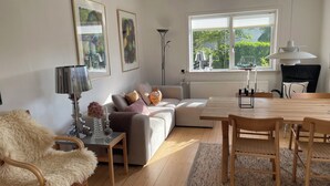 A living room with a sofa, a dining table, a lamp, and a chair. - Holiday Flat in Skagen town (Skagen)