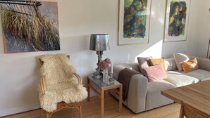 A living room with a sofa, a chair, a table, and wall art. - Holiday Flat in Skagen town (Skagen)