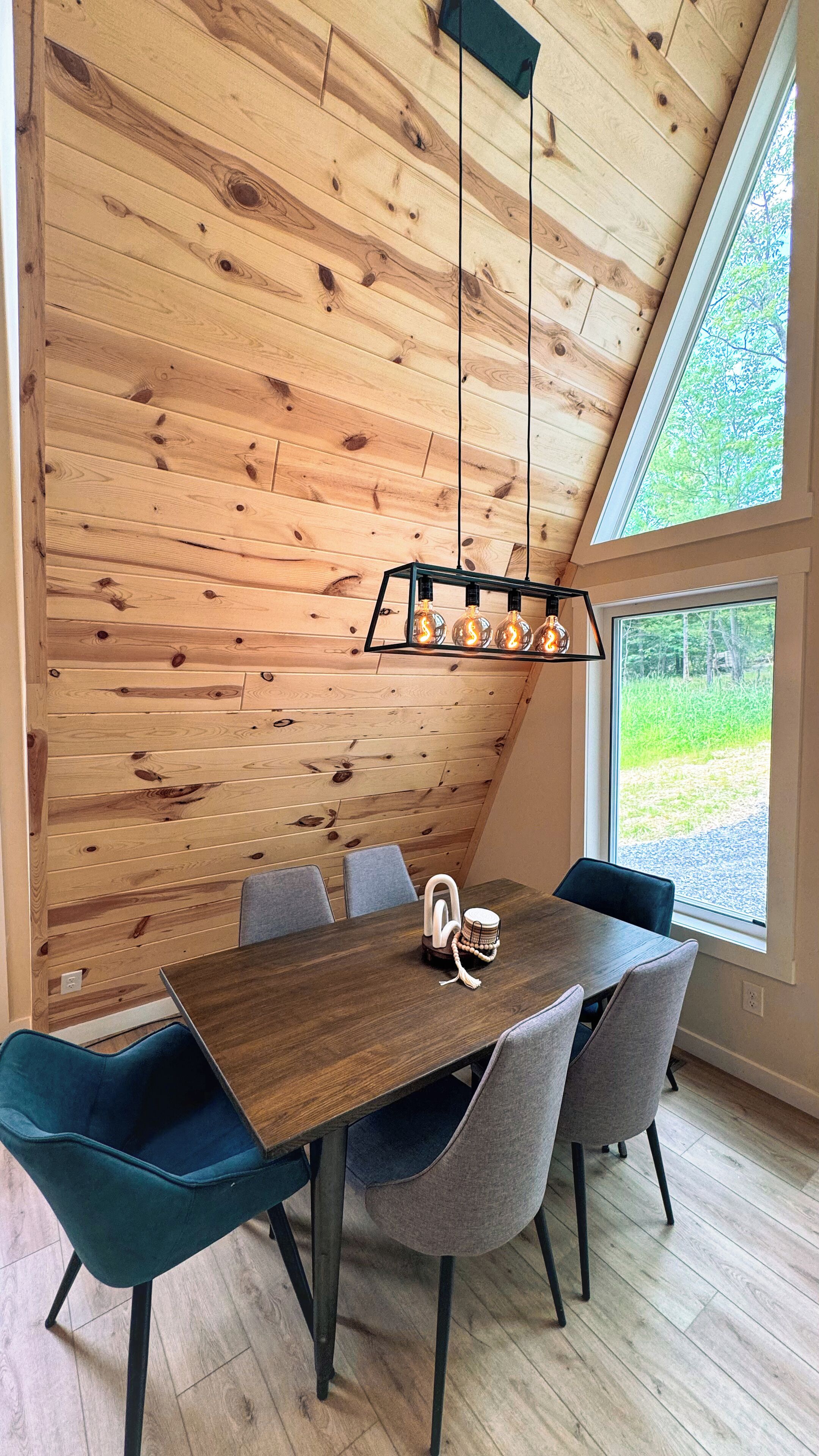 Un comedor con techo de madera, una mesa con sillas y vista a espacios verdes.