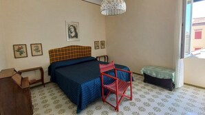 Quarto com cama, cadeira, mesinha e luminária pendente.