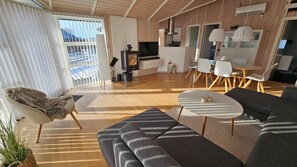 A modern living room with a sofa, a coffee table, and a TV. There is a dining area with chairs and a table.
