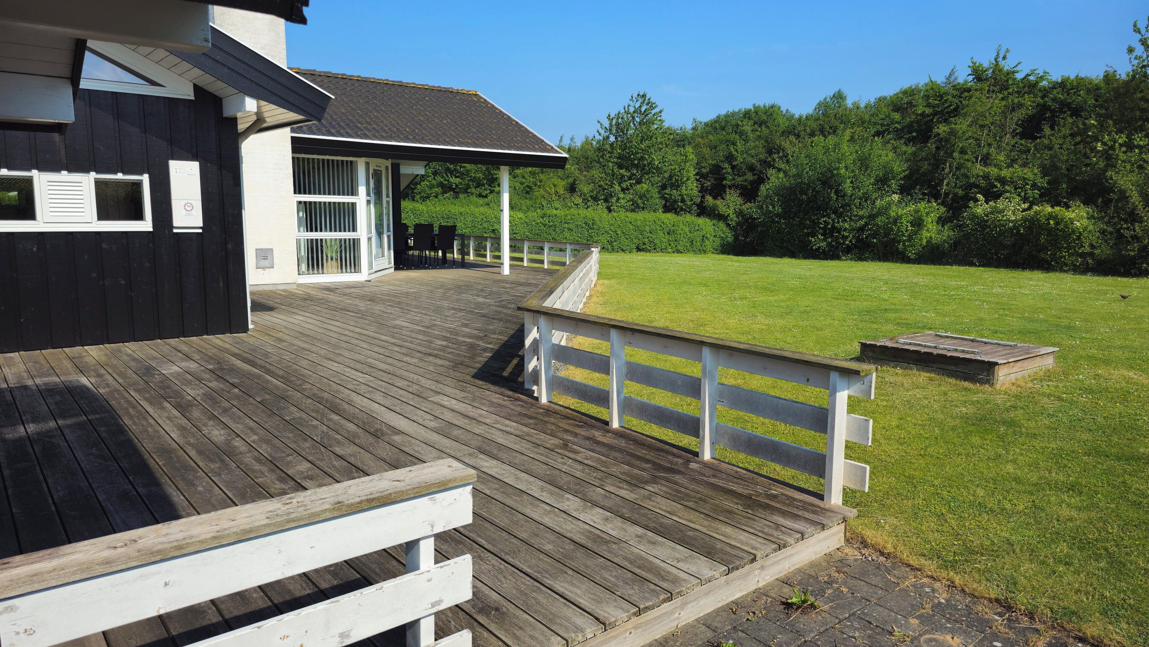 A wooden deck leading to a house with a covered porch and a grassy yard.