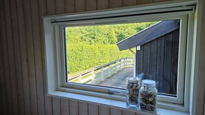 Une fenĂȘtre donnant sur une terrasse en bois et une forĂȘt.