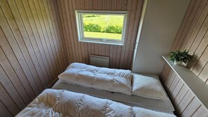 Une petite piĂšce aux murs lambrissĂ©s, avec un lit simple, une fenĂȘtre donnant sur un champ et un radiateur.