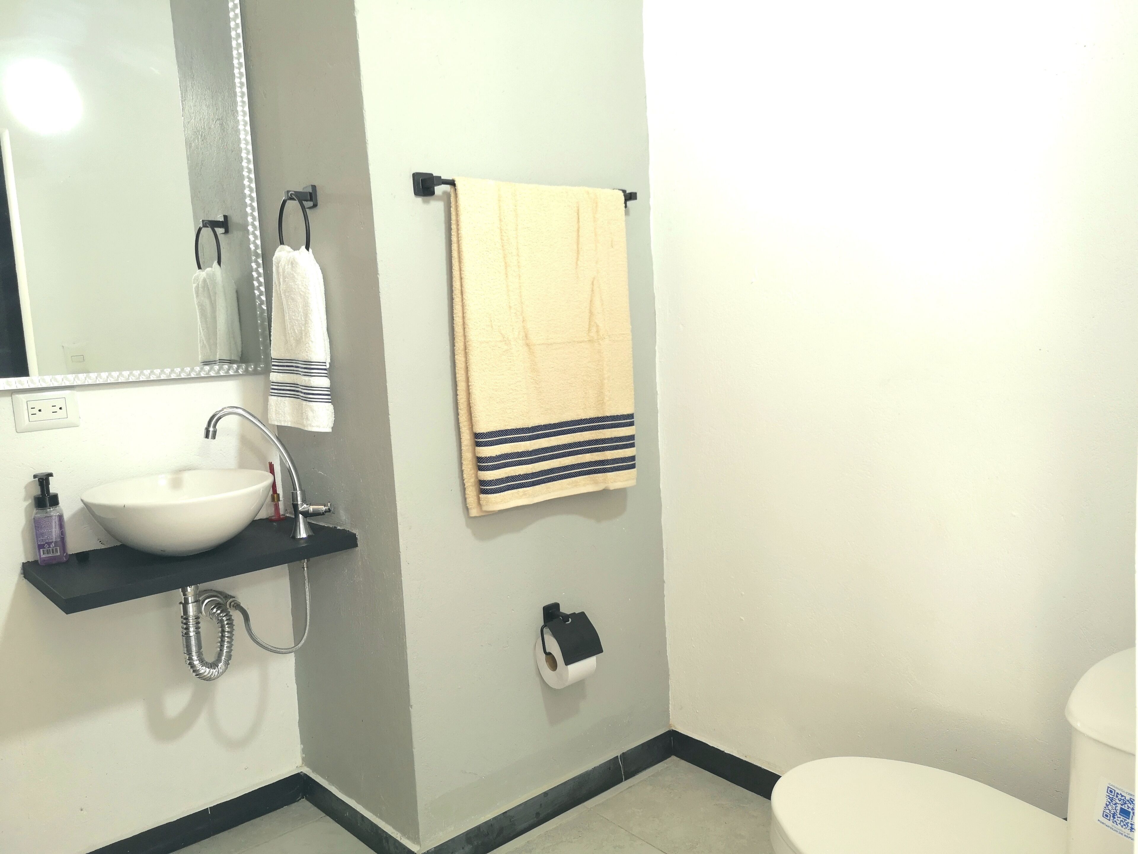 A bathroom with a white sink, a mirror, a towel rack with a striped towel, and a toilet.
