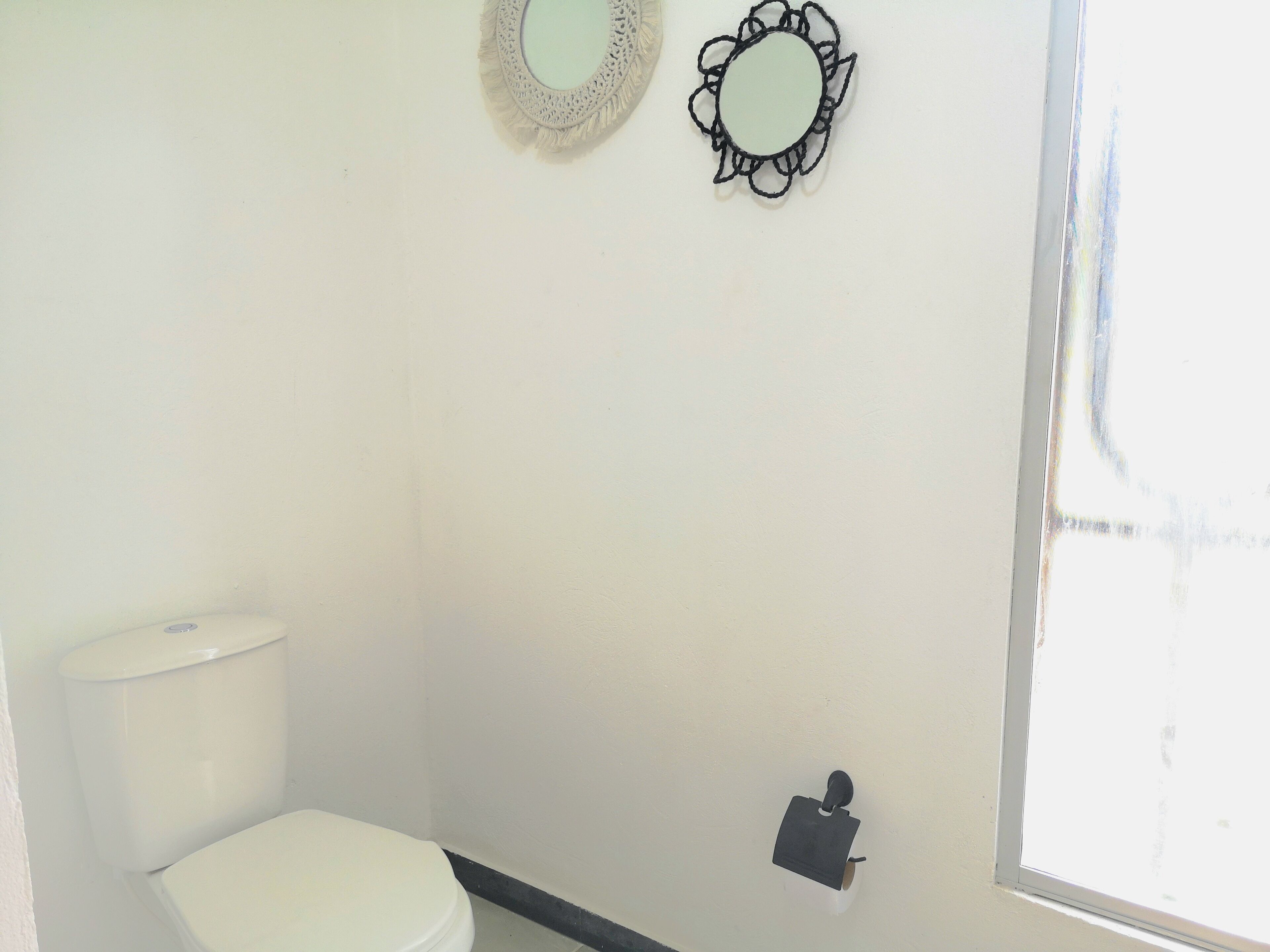 A small, clean bathroom with a toilet, a wall-mounted mirror, and a window.