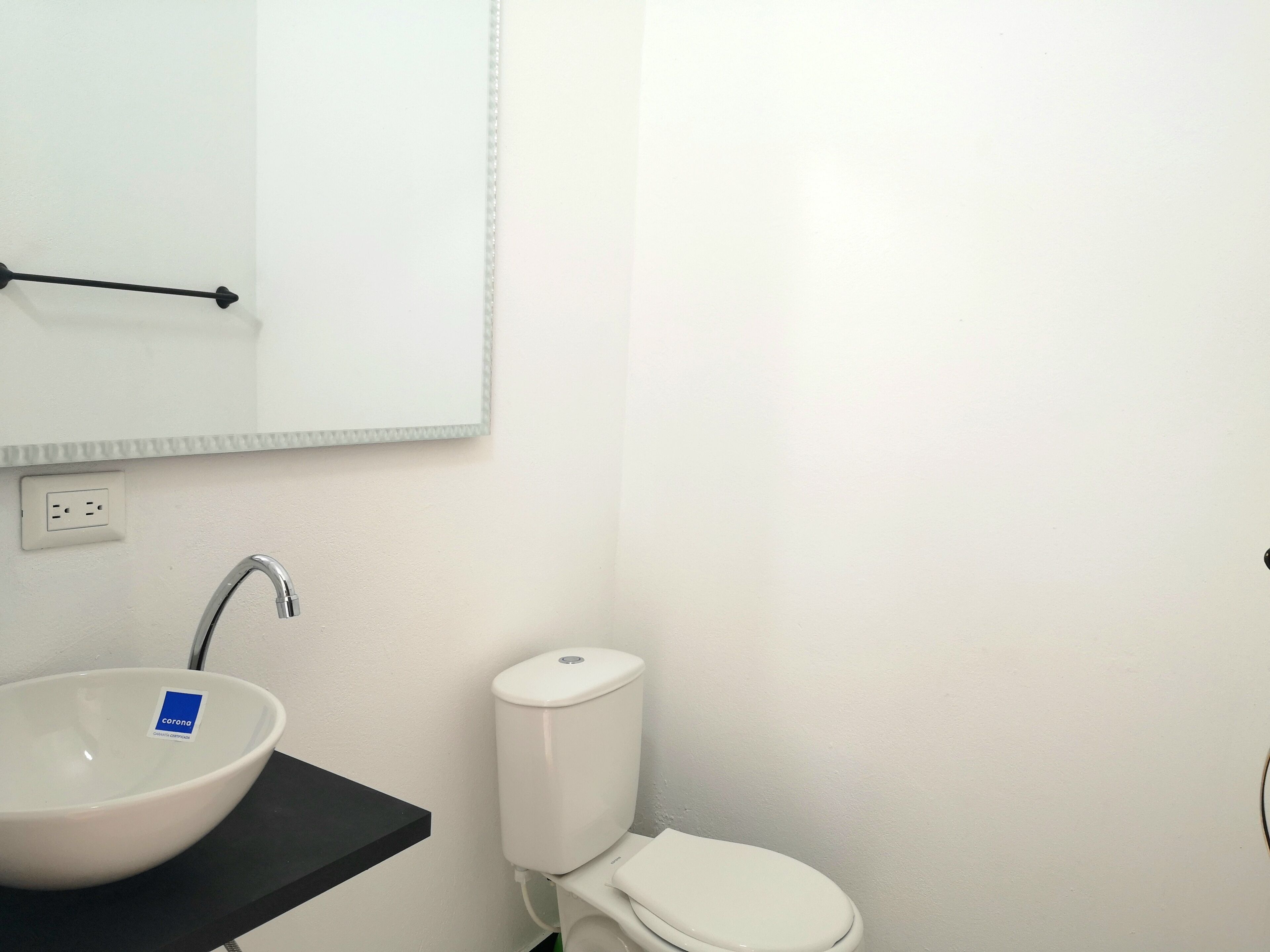 Un baño con un lavabo blanco, un espejo, una encimera negra, un inodoro blanco y una pared blanca.