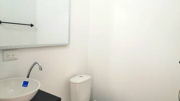 Un baño con un lavabo blanco, un espejo, una encimera negra, un inodoro blanco y una pared blanca.