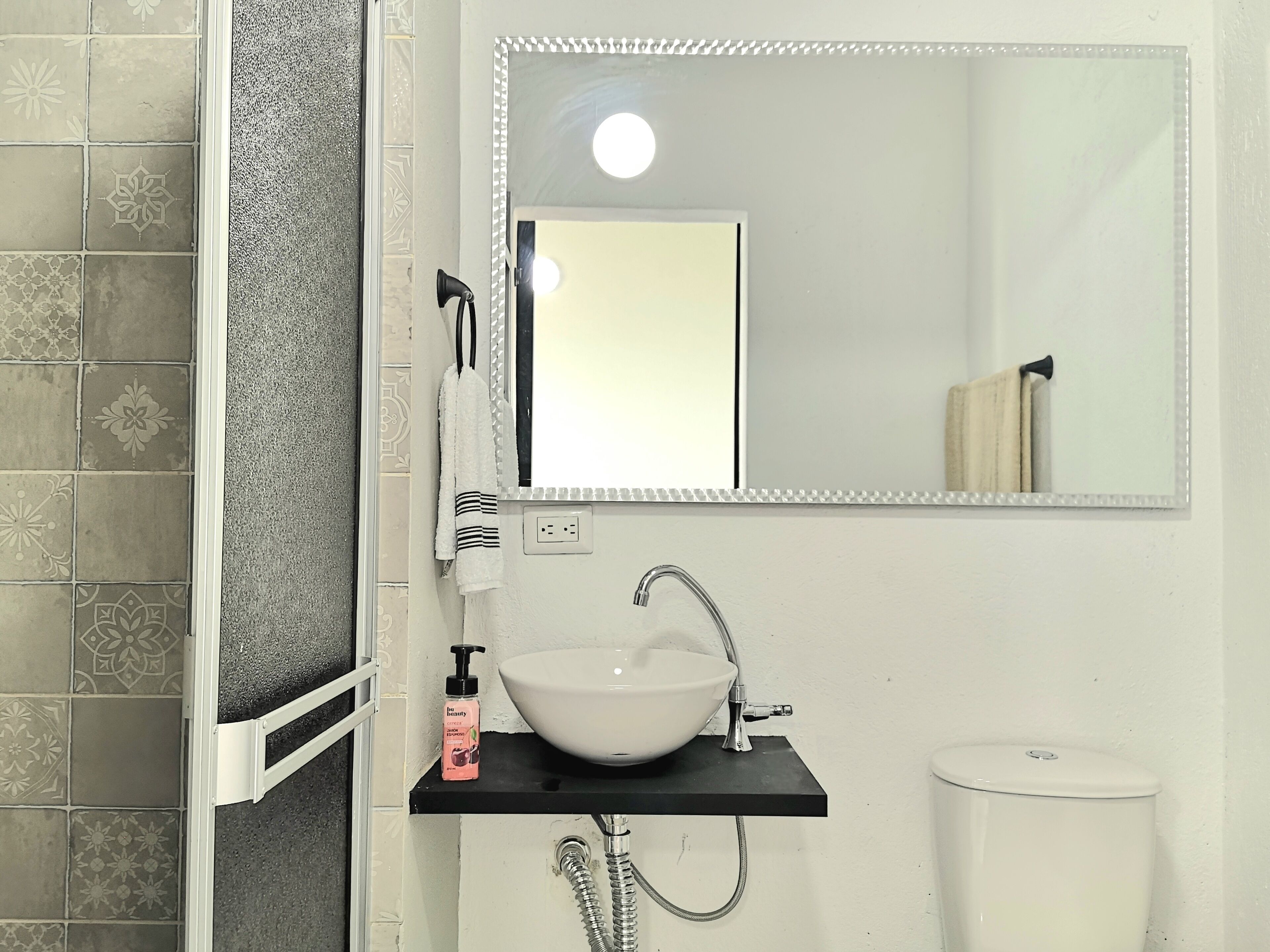 Un baño con lavamanos blanco, espejo y ducha.