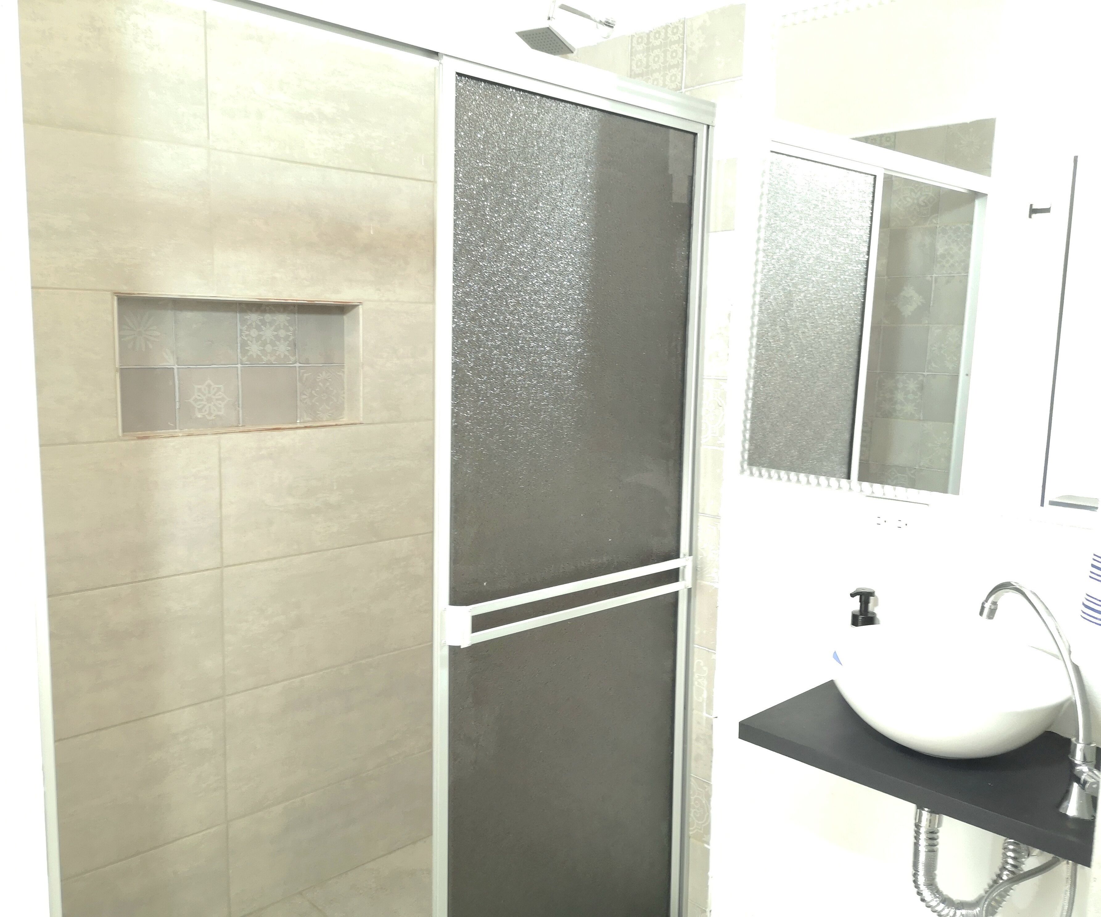 A bathroom with a shower enclosure, a sink with a mirror, and tiled walls.