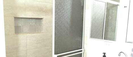 A bathroom with a shower enclosure, a sink with a mirror, and tiled walls.