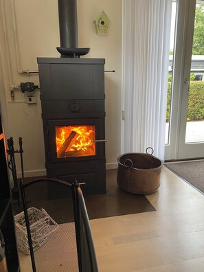 Ein Zimmer mit Kaminofen, einem Metallkübel und einem Stuhl.
