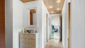 A hallway with a wooden floor, a white wall with a mirror, and a white cabinet with drawers. - Holiday house close to the beach. (Brenderup Fyn)
