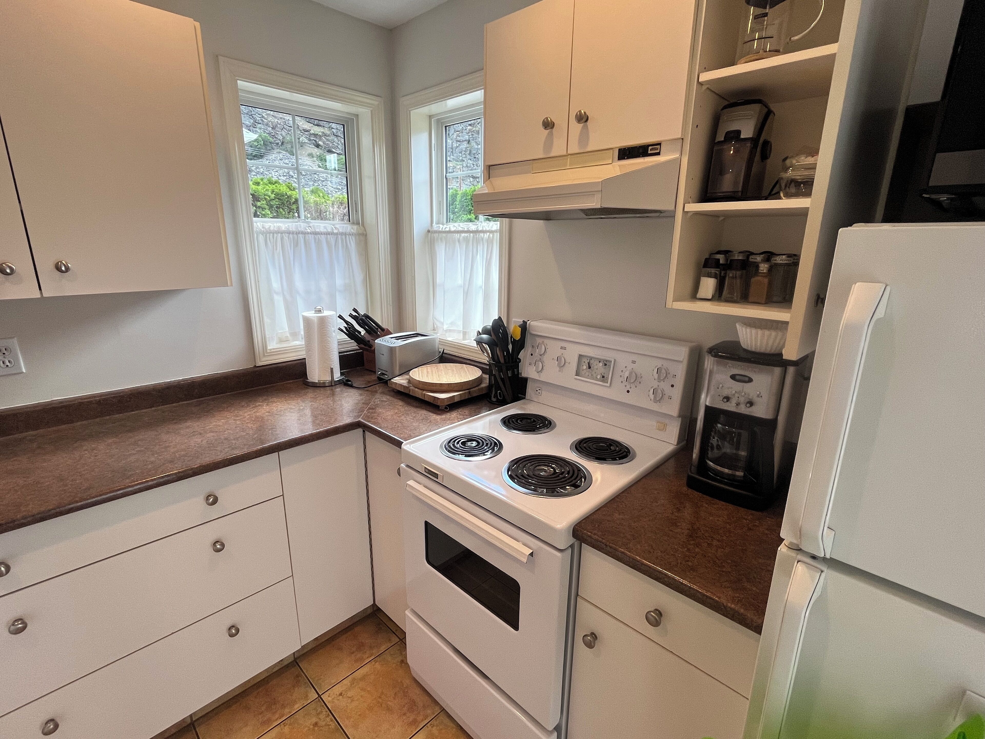 Una cocina con armarios blancos, estufa, refrigerador y cafetera.