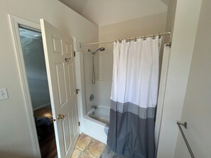 A bathroom with a bathtub, a shower curtain, and a door leading to another room. - Beach Front, Lake, Fishing, Canoe, Paddle boards #4 (Oliver)