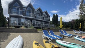 A modern building with multiple balconies and a sandy beach area with lounge chairs and kayaks. - Beach Front, Lake, Fishing, Canoe, Paddle boards #4 (Oliver)