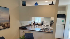 A compact kitchen with a dining area, a white refrigerator, a microwave, and a stove. - Beach Front, Lake, Fishing, Canoe, Paddle boards #4 (Oliver)