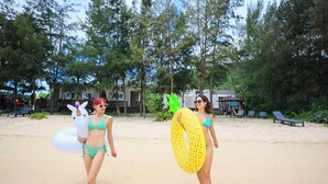 A sandy beach with lounge chairs and a building in the background. - Le Grand Bleu (Tatsugo)