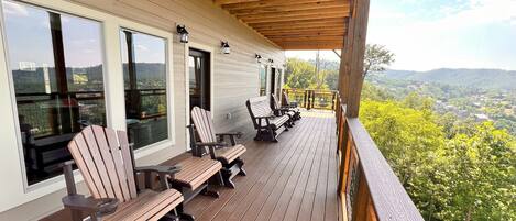A wooden deck with outdoor seating and large windows overlooking a scenic landscape.