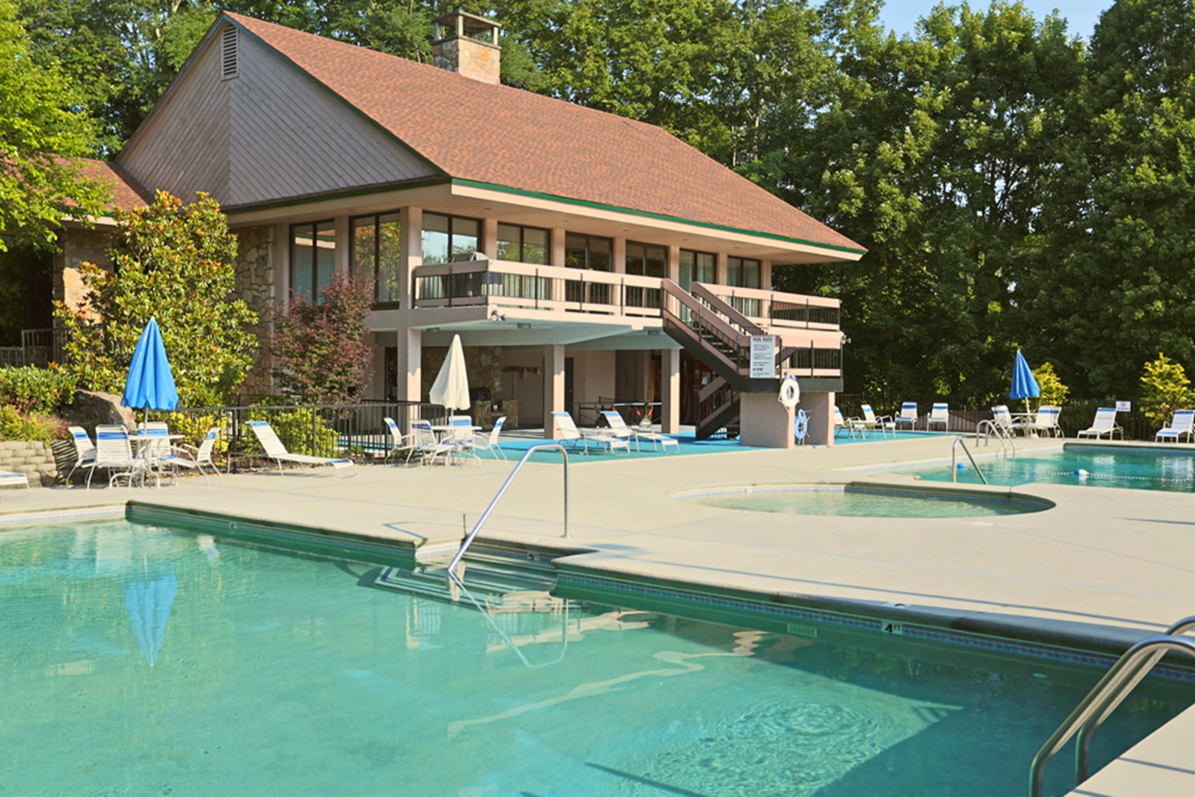 Un espace piscine avec des chaises longues et des parasols, un bâtiment doté d’un balcon et un escalier menant à l’étage supérieur.