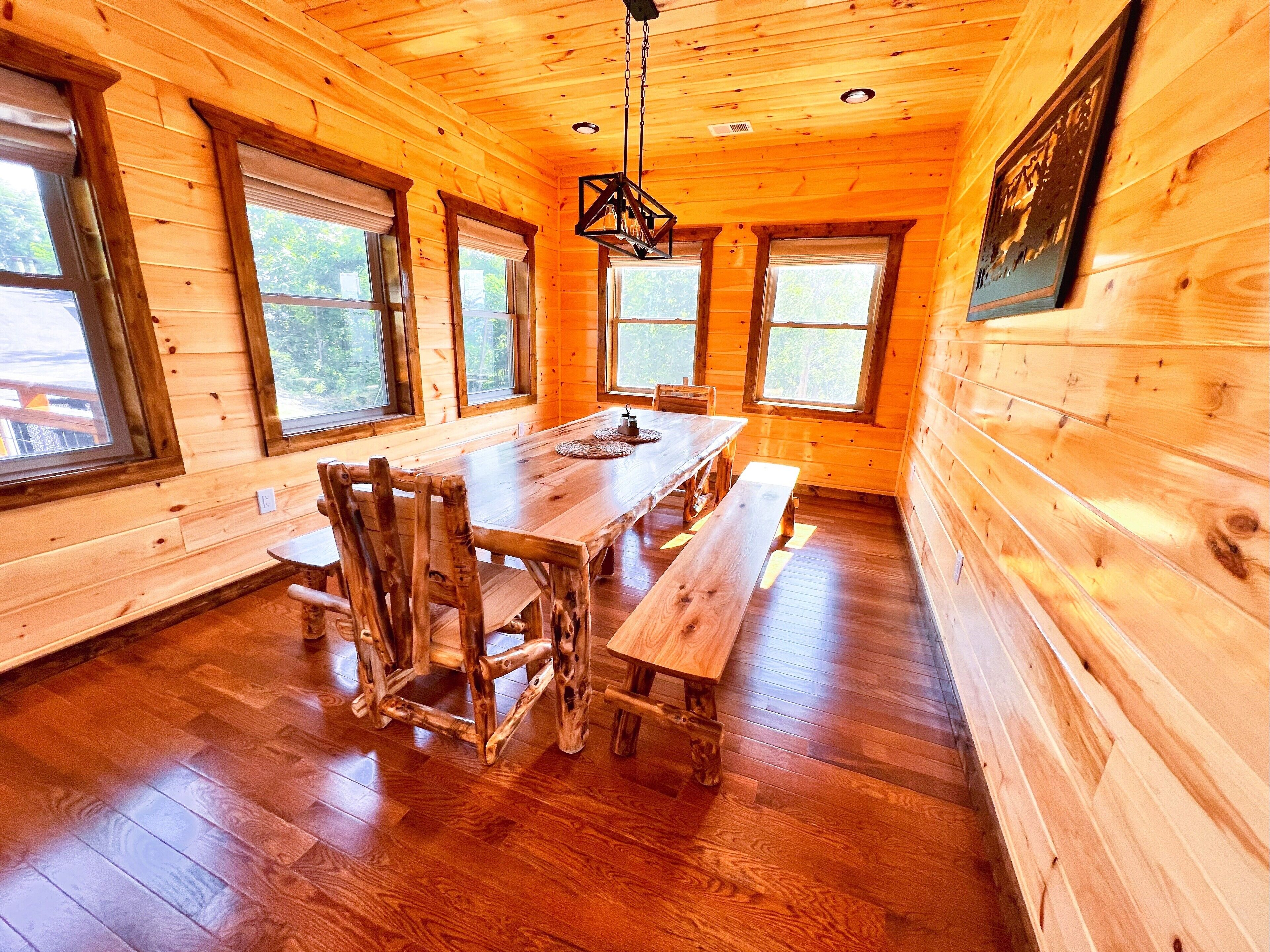 A wooden cabin interior with a dining table, benches, and large windows.