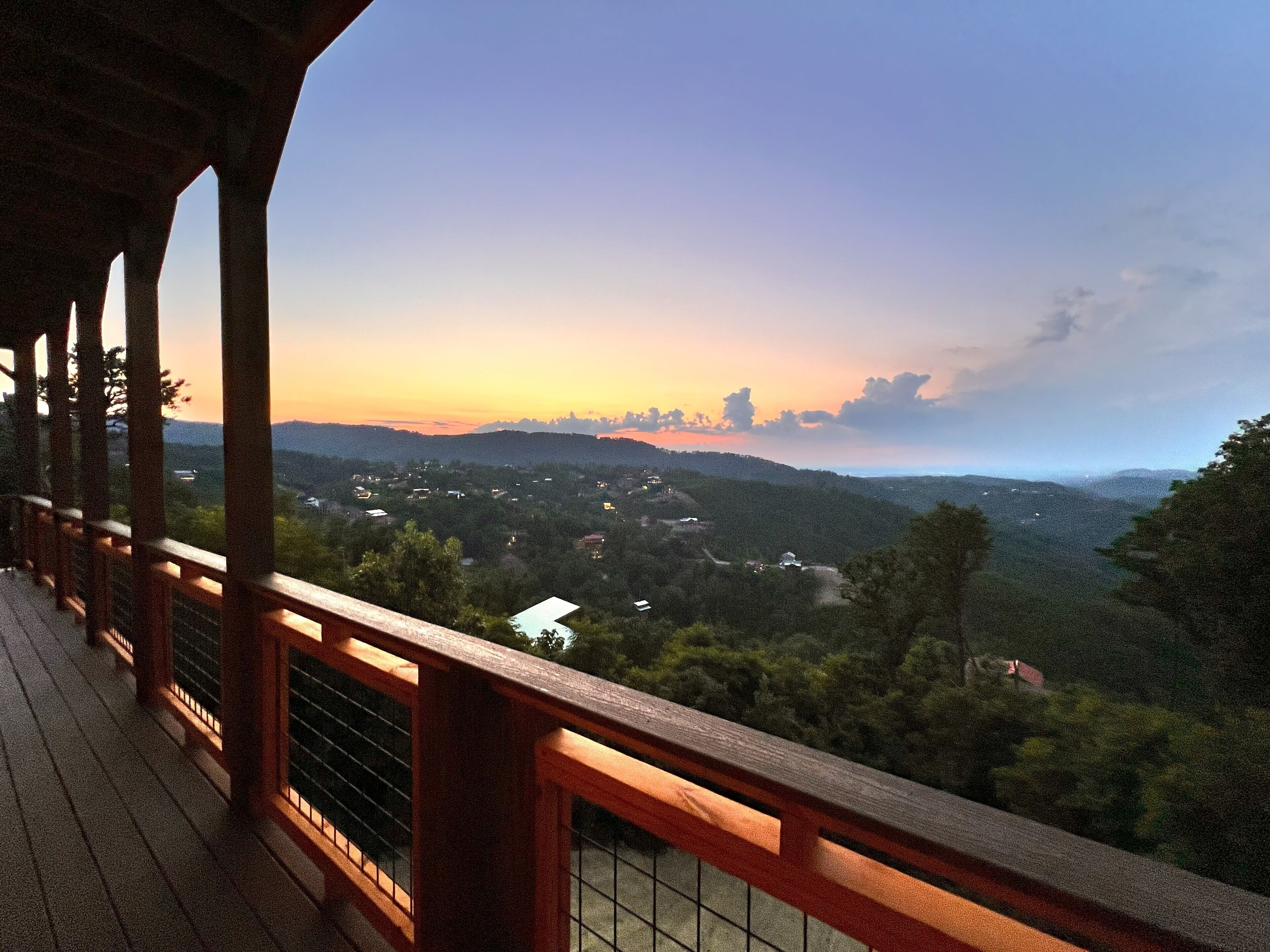 A wooden deck with a view of a valley and distant mountains during sunset.