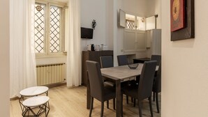 A dining area with a table and chairs, a television mounted on the wall, and a window with curtains. - GuestHost - Trastevere Three Luxury Rooms (Roma)