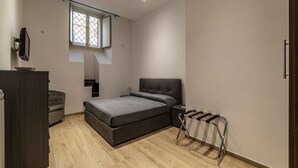A bedroom with a bed, a desk, a chair, a wardrobe, a window, and a hanging rack. - GuestHost - Trastevere Three Luxury Rooms (Roma)
