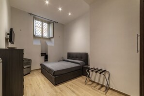A bedroom with a bed, a desk, a chair, a wardrobe, a window, and a hanging rack.