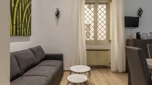 A living room with a sofa, two round tables, a TV, and a window with curtains. - GuestHost - Trastevere Three Luxury Rooms (Roma)
