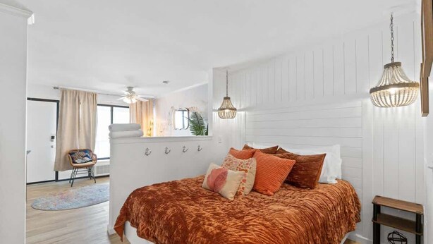Een slaapkamer met een groot bed, een houten nachtkastje, een hanglamp en uitzicht op een balkon.