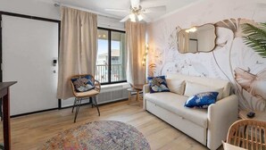 Een woonkamer met een bank, stoelen, een plafondventilator en een groot raam met gordijnen.