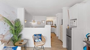 Een moderne keuken met witte kastjes, een centraal eiland en een eethoek met een stoel en tafel.