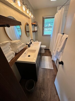 A modern bathroom with two sinks, a large mirror, a shower curtain, and a window with blinds. - Cozy on Campus! Keep it simple at this centrally-located place on the KU Campus. (Lawrence)