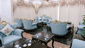 A luxurious room with a chandelier, blue upholstered chairs, a black coffee table, and cream-colored curtains. - Senior Hotel (Can Tho)