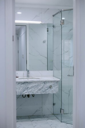 A bathroom with a marble sink, glass shower enclosure, and white marble walls. - Senior Hotel (Can Tho)